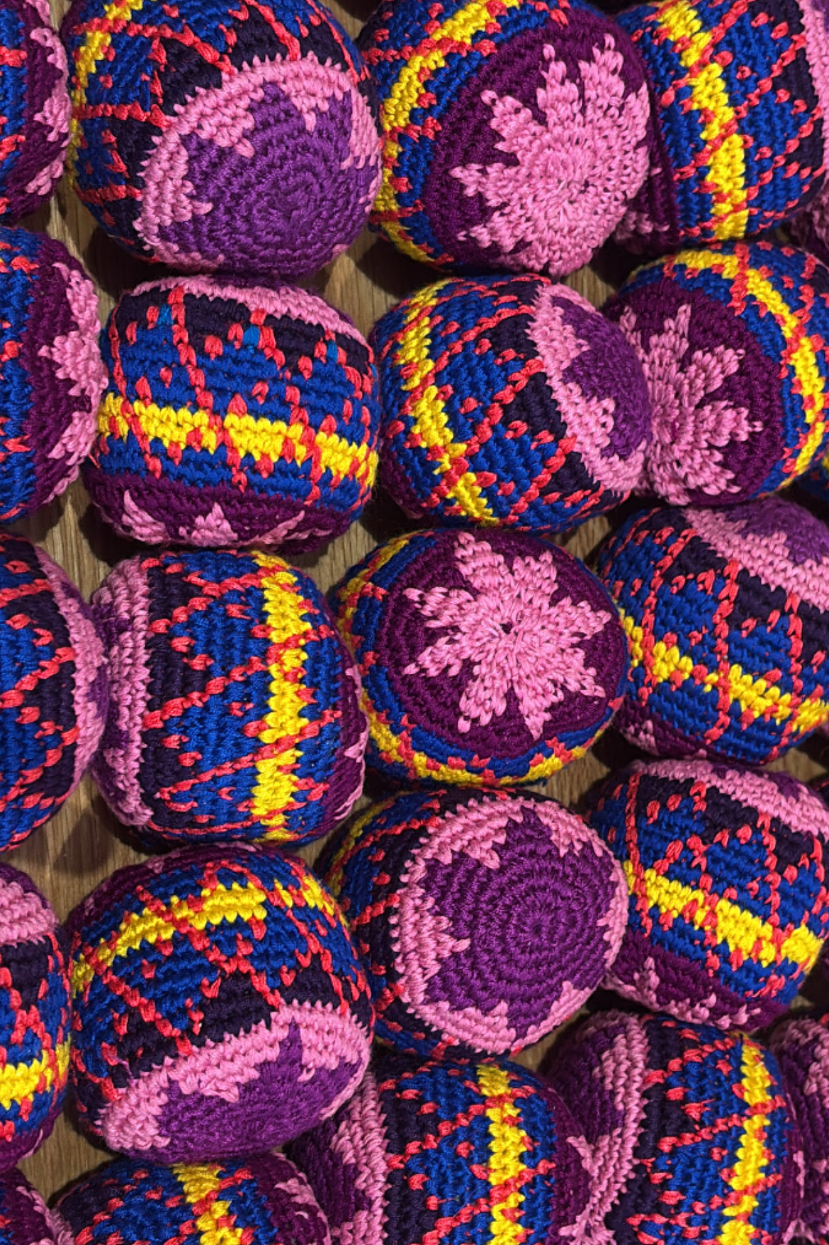 A close-up, top-down view of multiple handmade crocheted or knitted round bags in a repeating pattern of purple, pink, blue, and yellow.