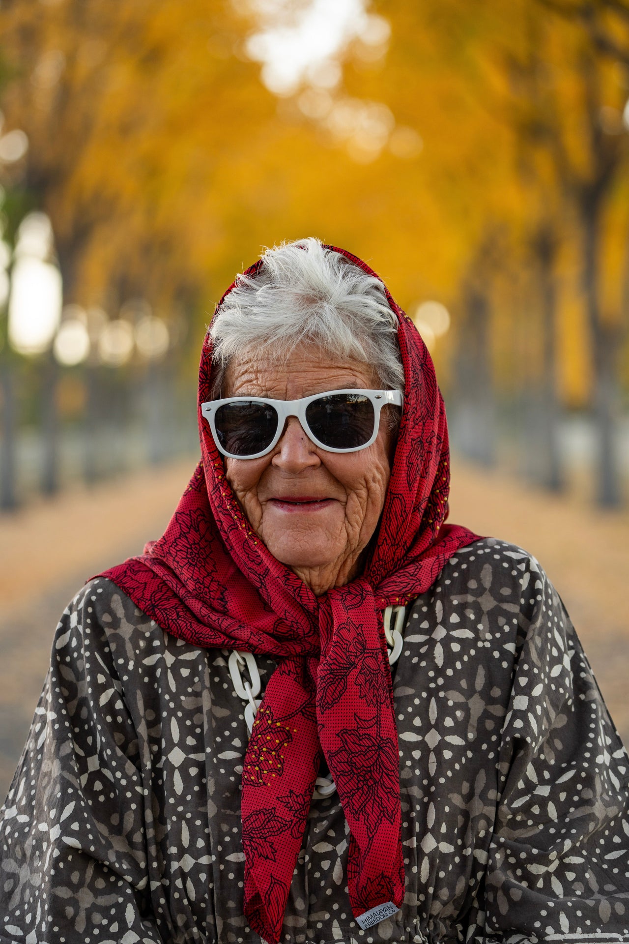 woman wearing a red headscarf and sunglasses with a blurred autumn background